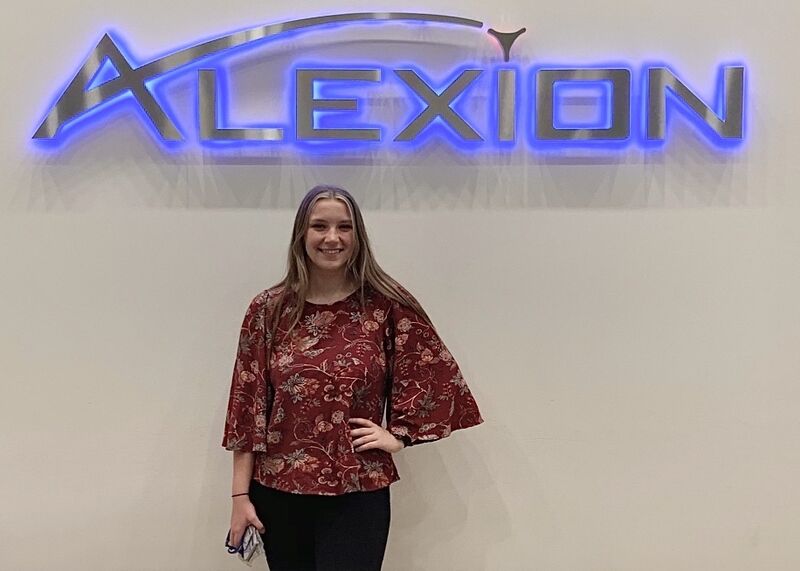 A woman standing in front a logo of Alexion