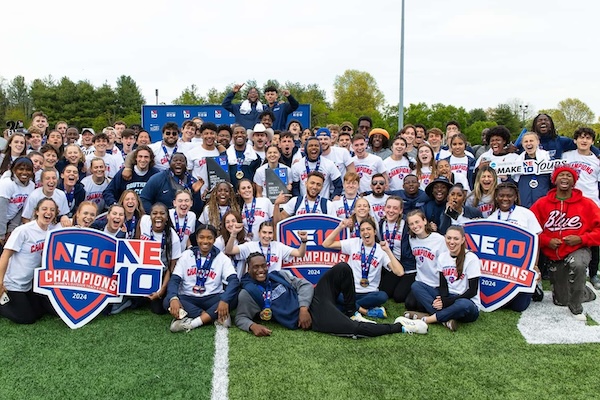 Women's track and field together holding NE10 championship signs