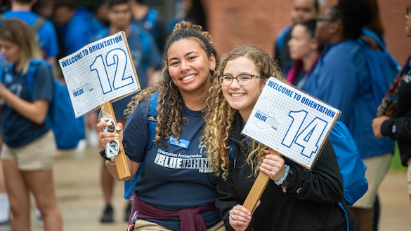 Two women holding Welcome to Orientation signs