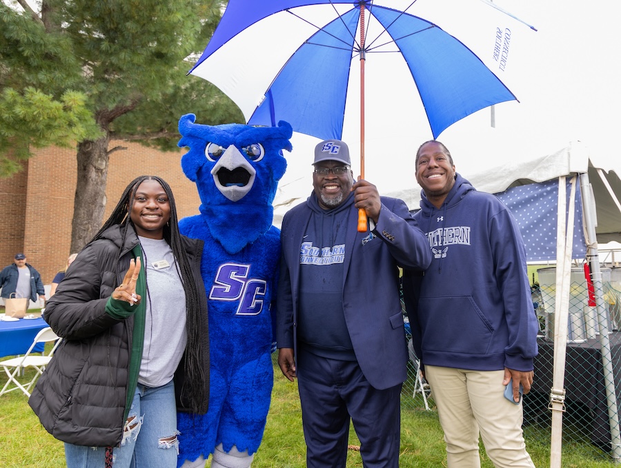 Dr. Dwayne Smith holding an umbrella with staff, alumni, and the Owl mascot