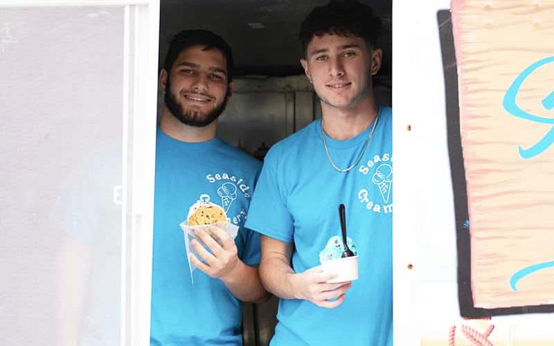 Benjamin and Brandon Foligno, '25, hold ice cream treats in the window of their Seaside Creamery ice cream truck