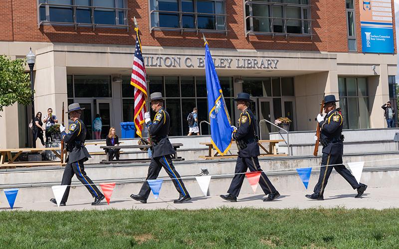 a police honor guard carries the state and US flags in front of Buley Library