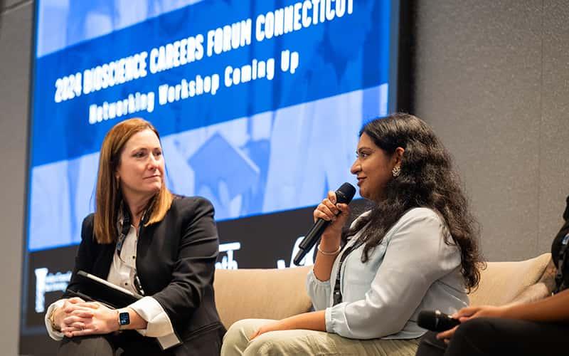 two women speak on a panel in front of a blue screen that says "bioscience careers forum"