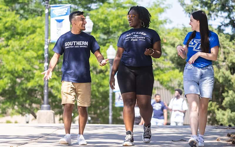 three students in SCSU t-shirts walk together on campus