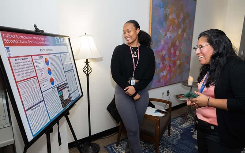 a student shows her poster project to a staff member