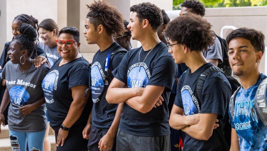 Students wearing University Access Programs shirts and smiling outside of the Adanti Student Center.