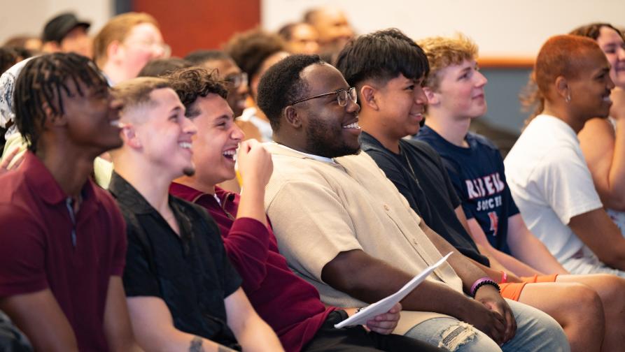 Audience watches a presentation, smiling and laughing.