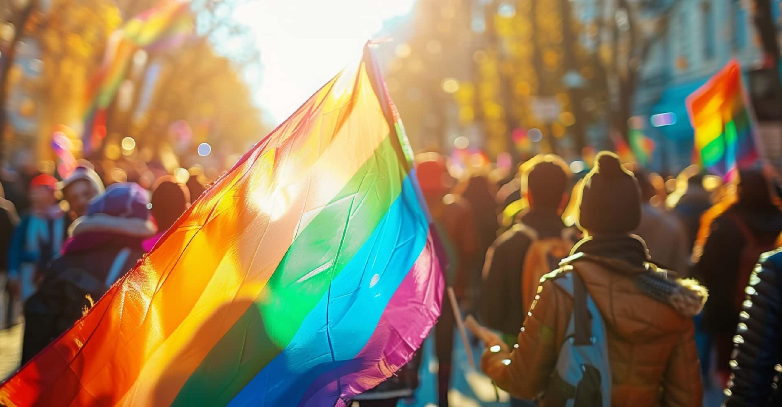 a street scene with a crowd of people holding a couple of LGBT Pride flags