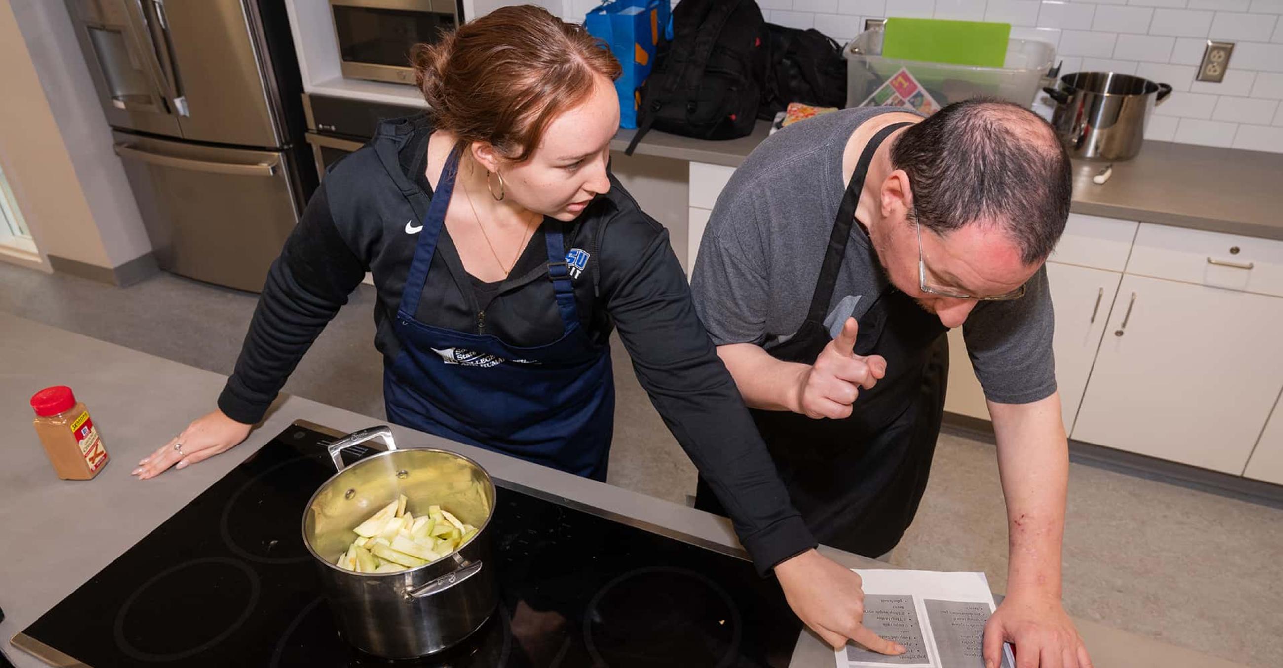 one person appears to show another a recipe or set of cooking instructions as they both stand in front of a stove