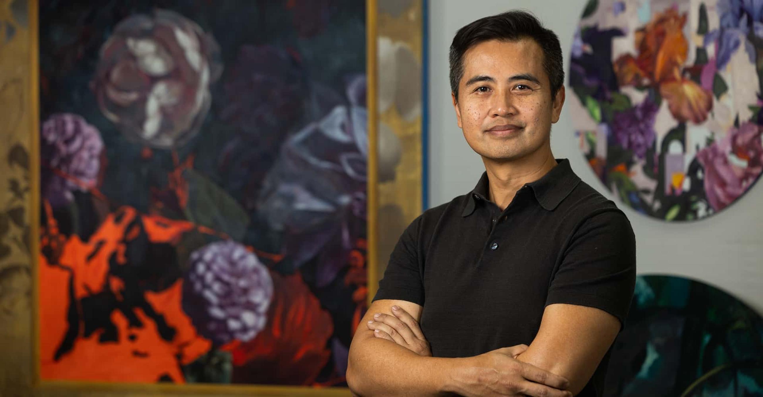 Thuan Vu stands in front of two of his paintings